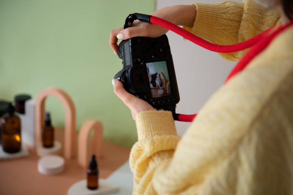 A close-up of hands holding a camera taking a photo of cosmetic products, illustrating detailed product imaging.