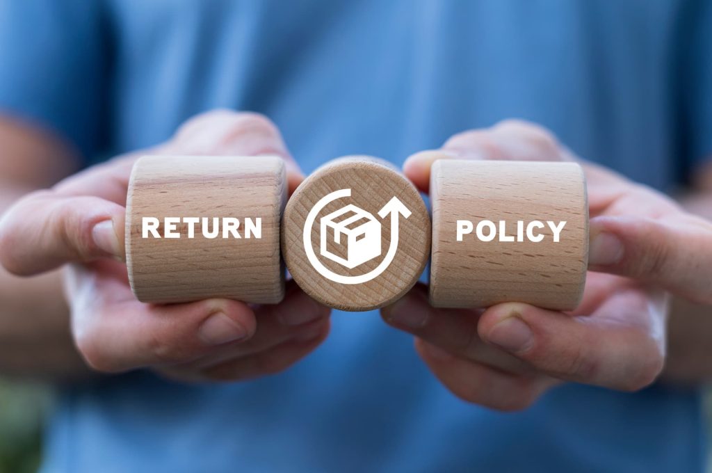 Hands holding wooden blocks with 'RETURN' and 'POLICY' facing the camera, symbolizing the importance of a clear return policy.