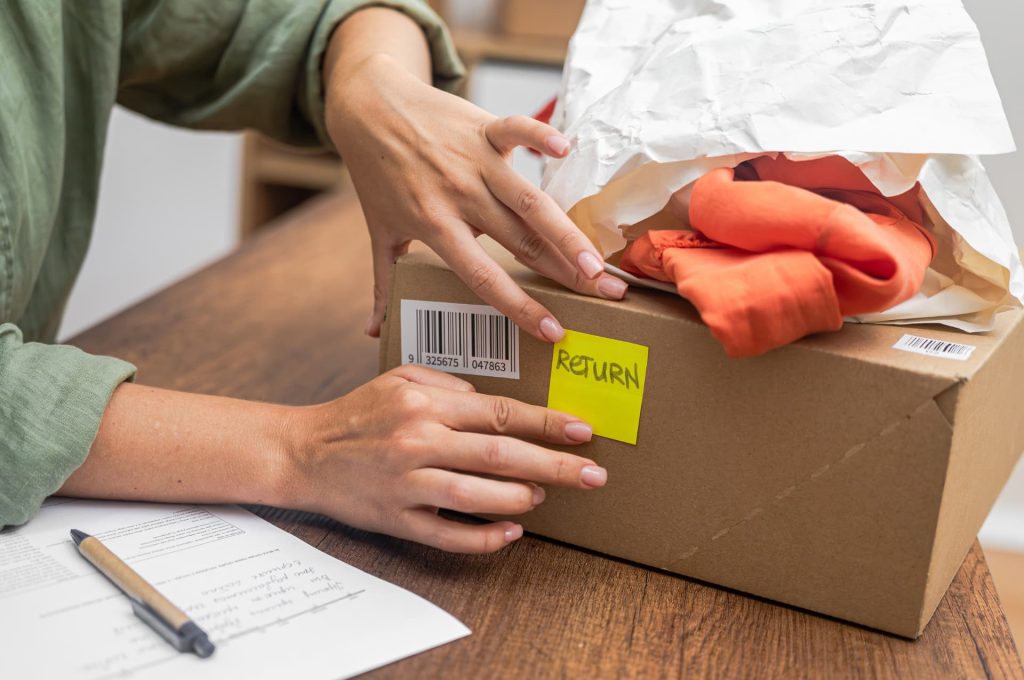 A person packing a red item into a box with a 'RETURN' label, showing a customer preparing a return shipment.