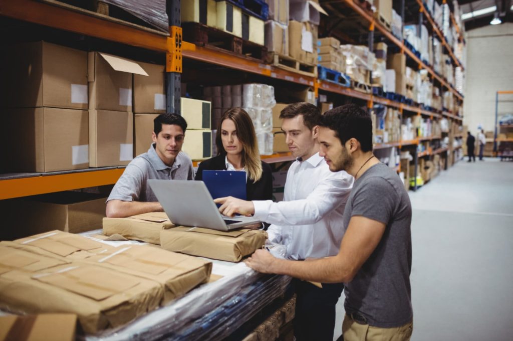 A team analyzing data on a laptop in a warehouse environment, showcasing the collaborative effort in managing ecommerce fulfillment operations.