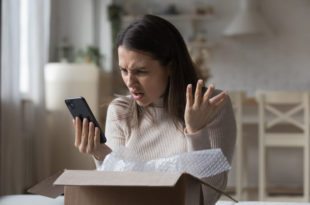 A frustrated customer looks at her phone next to an open package, depicting a negative reaction to an online order.