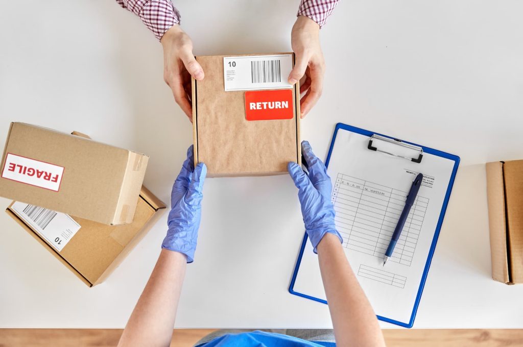 A top-down view of hands with gloves handling a returned package, signifying safe and hygienic handling of returns.